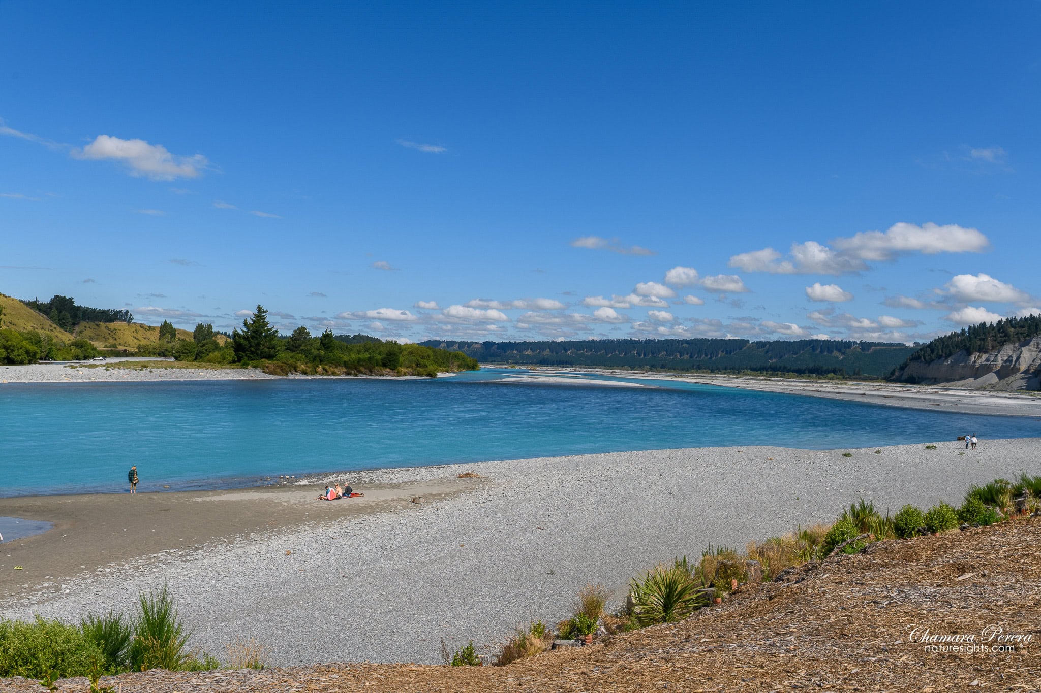 Visitors on wide gravel bank beside turquoise Rakaia River on a clear summer day New Zealand